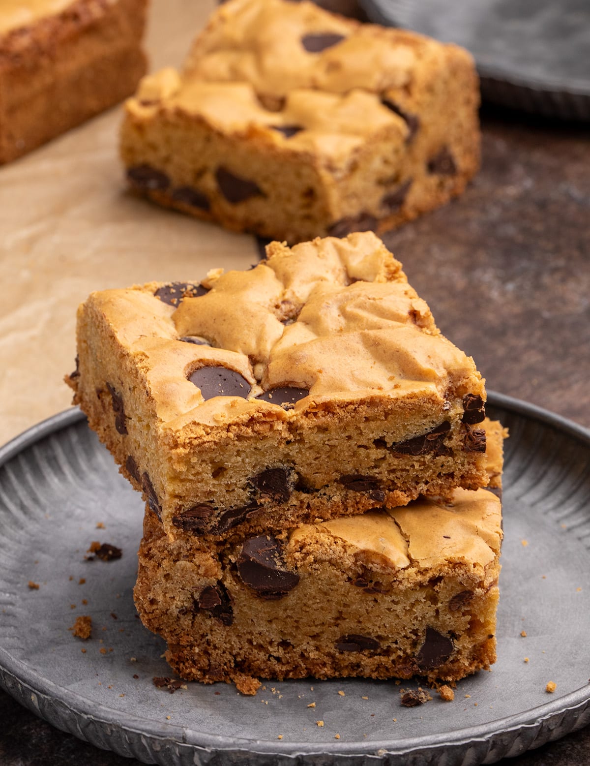 Two stacked chocolate chip cookie bars on a dark plate with more cookie bars in the background.