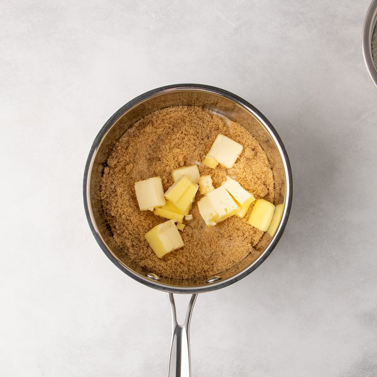Overhead view of brown and white sugars and chunks of butter in a stainless steel saucepan.