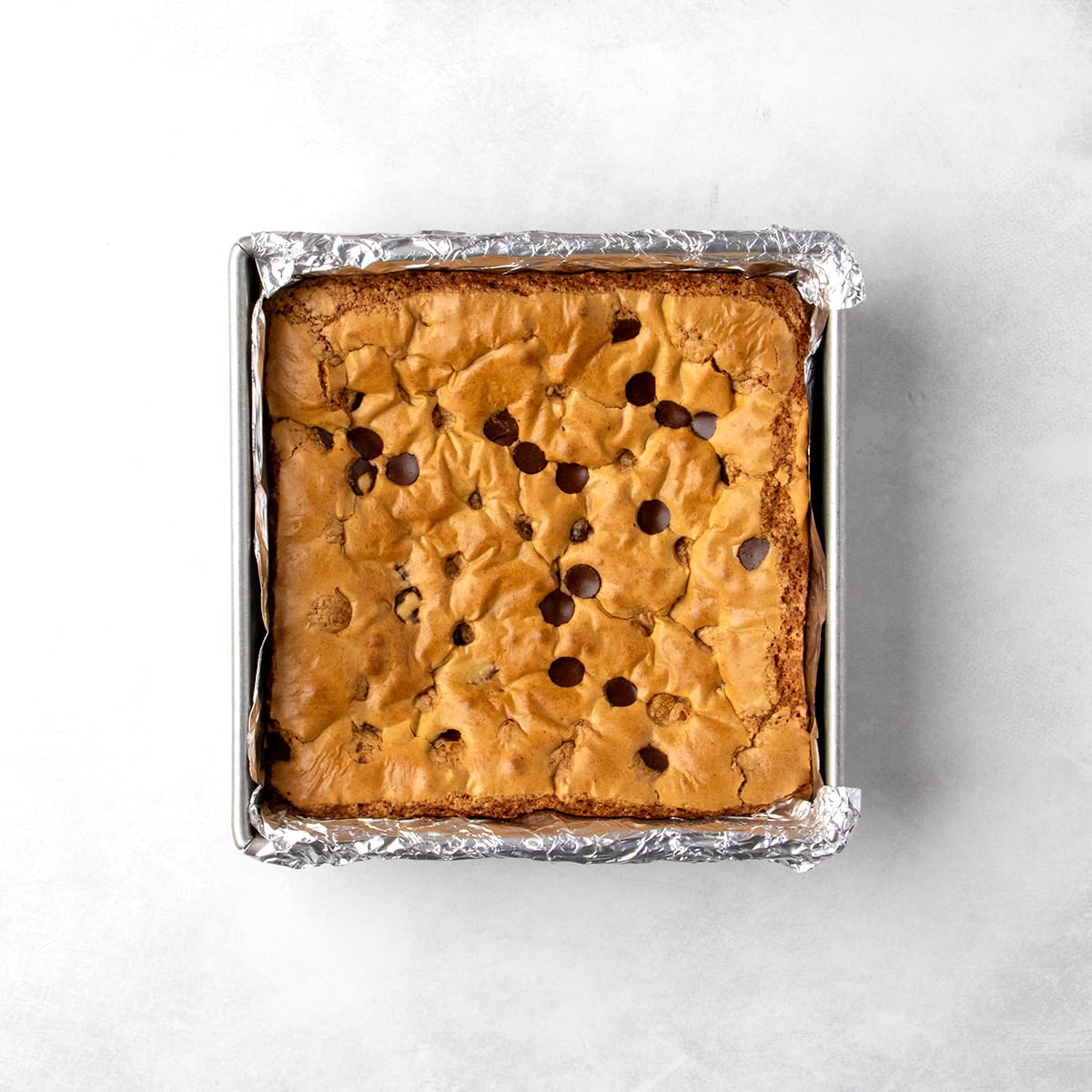 Overhead view of a uncut baked square cookie bar with crackly top in a foil-lined pan.