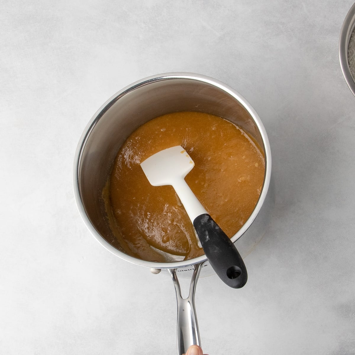 Overhead view of melted sugars and butter in a saucepan with a white spatula, with the saucepan tilted to the side slightly