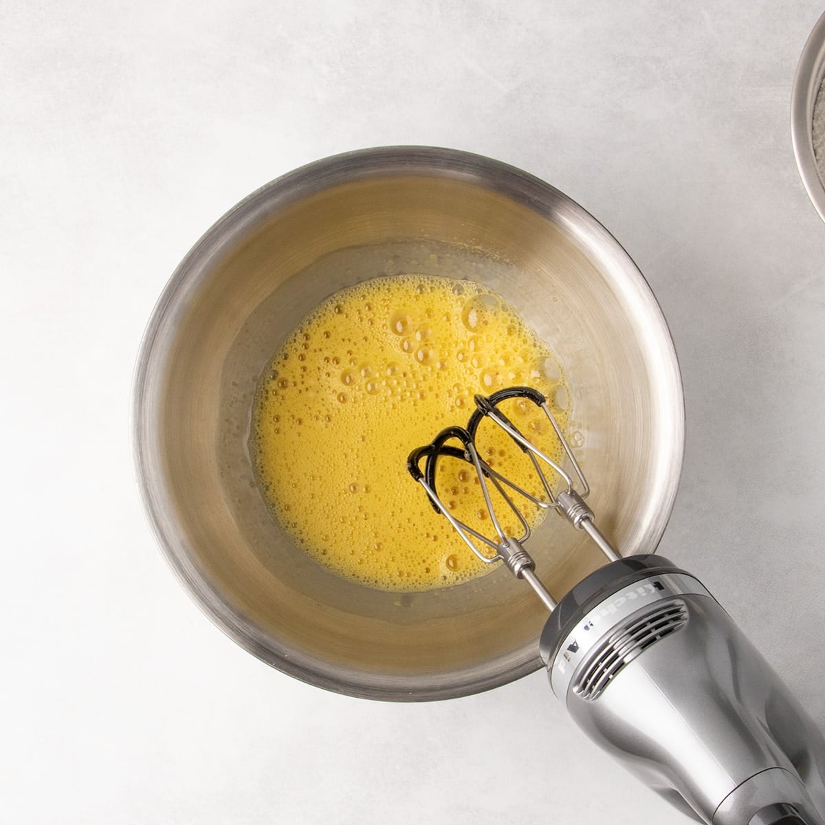 Overhead view of beaten eggs in a metal mixing bowl with a hand mixer.