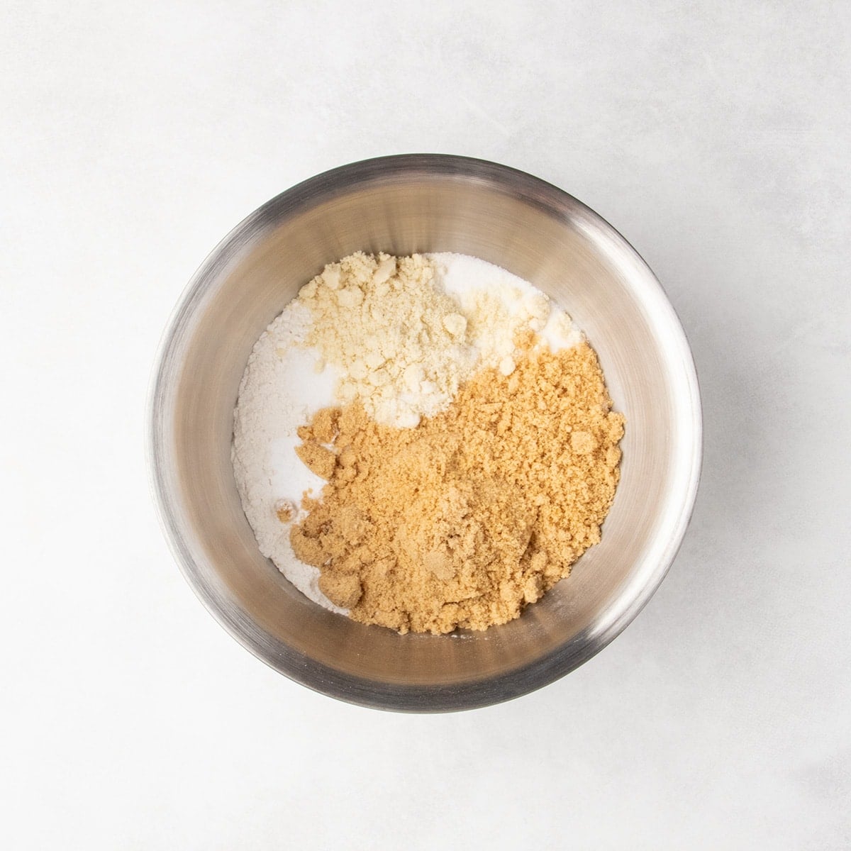 Metal mixing bowl with separate piles of white and pale tan and light brown dry ingredients.