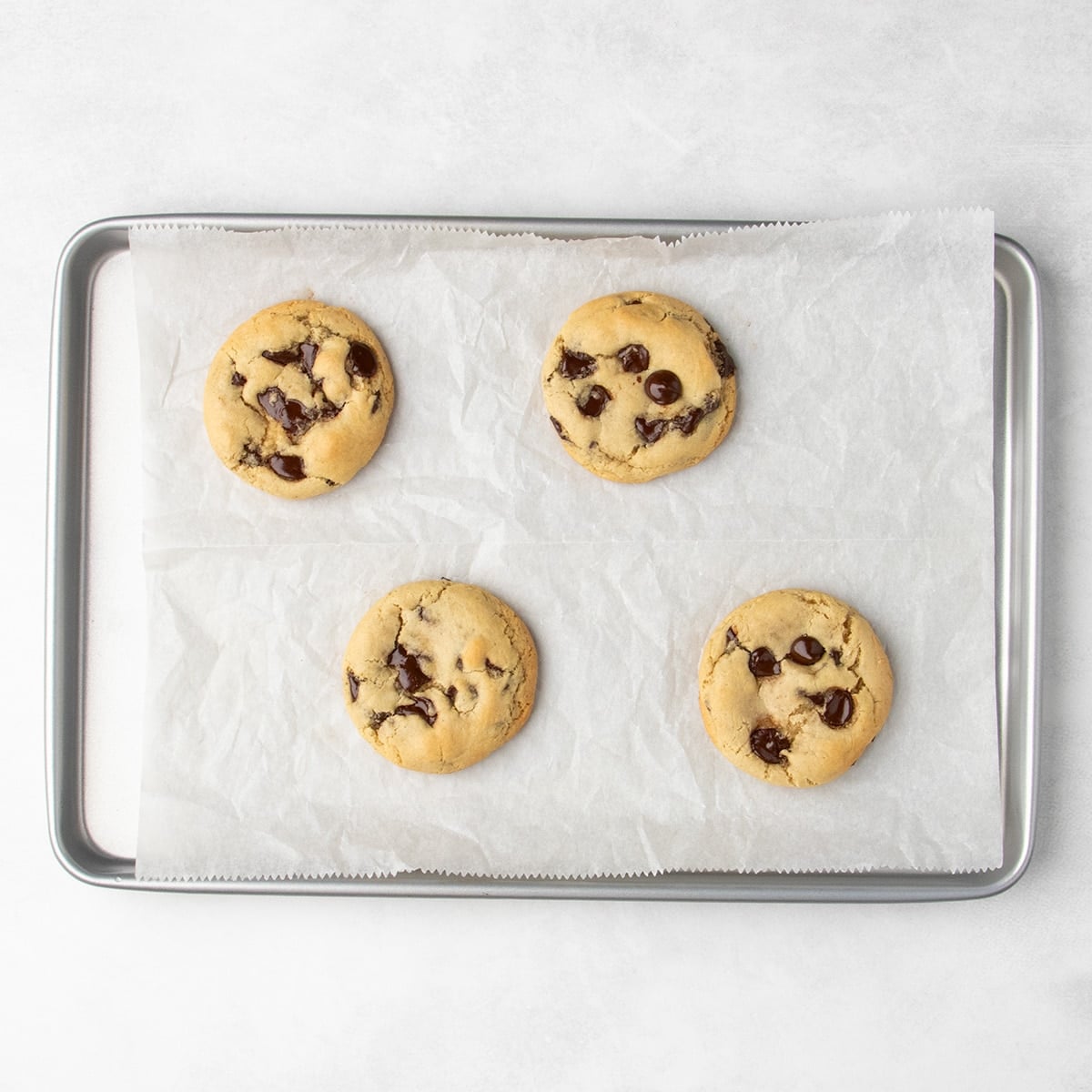 Four evenly spaced baked chocolate chip cookies on a parchment-lined baking sheet.
