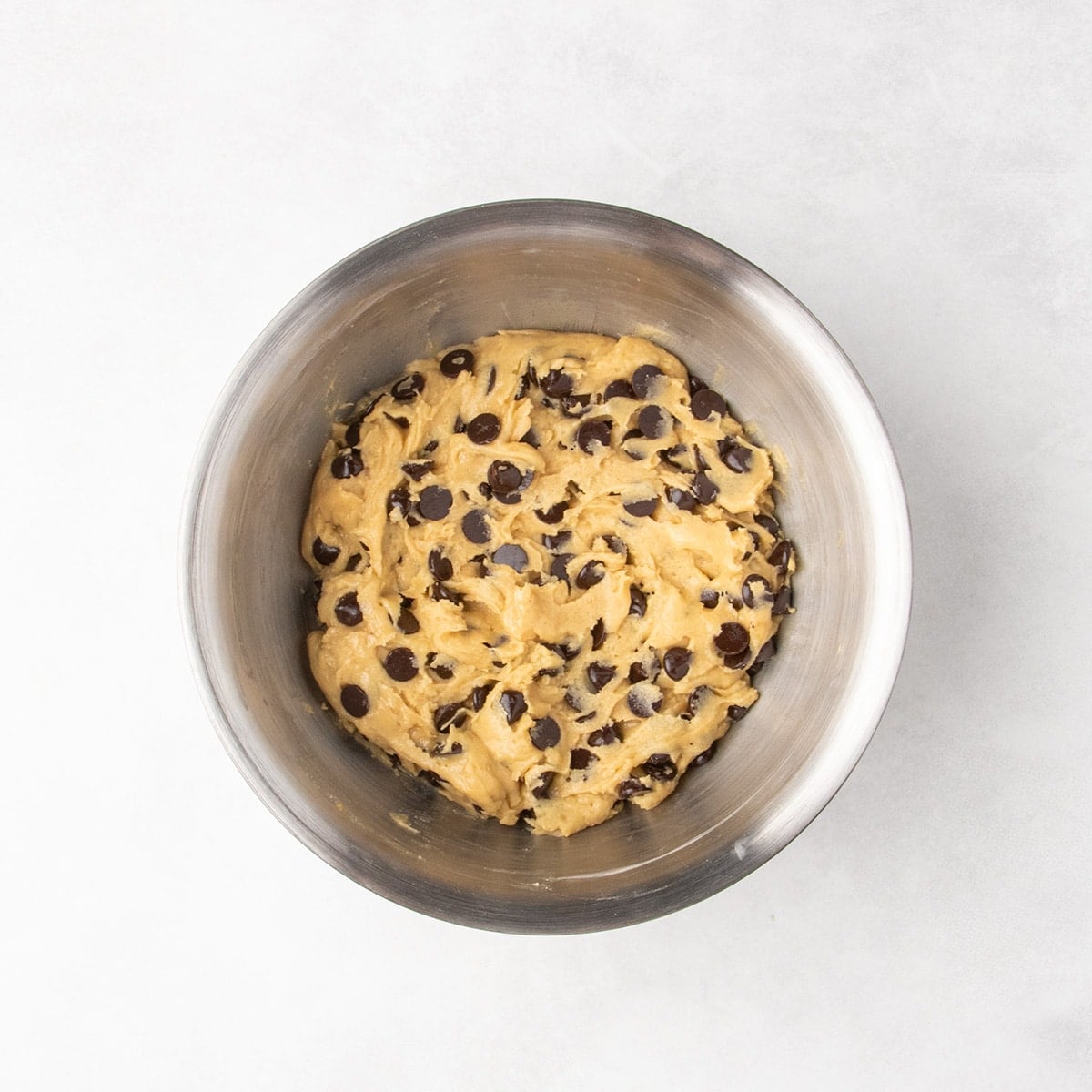 Soft raw chocolate chip cookie dough in a metal mixing bowl.