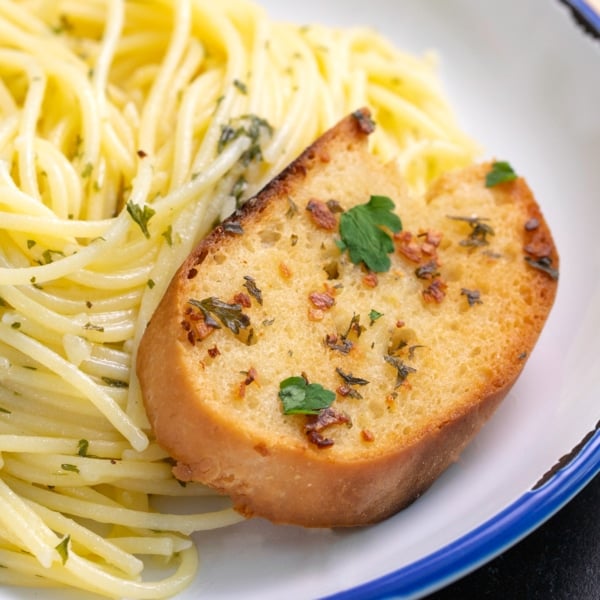 closeup image of one slice of gluten free garlic bread with toasted minced garlic and parsley leaves on bed of spaghetti