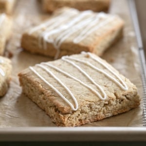 closeup of square gluten free oatmeal bars on brown paper on baking tray with white icing drizzle on top of each