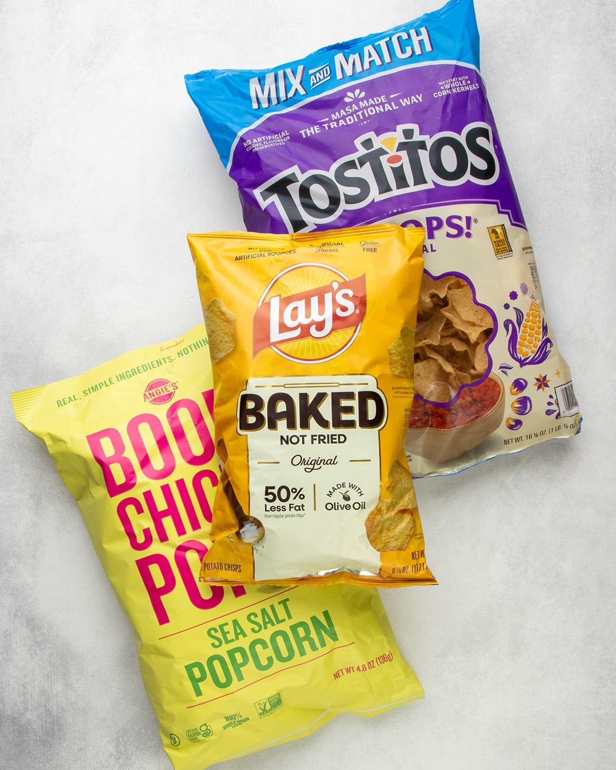 Bags of Angie’s Boomchickapop sea salt popcorn, Lay’s Baked Original potato crisps, and Tostitos tortilla chips.