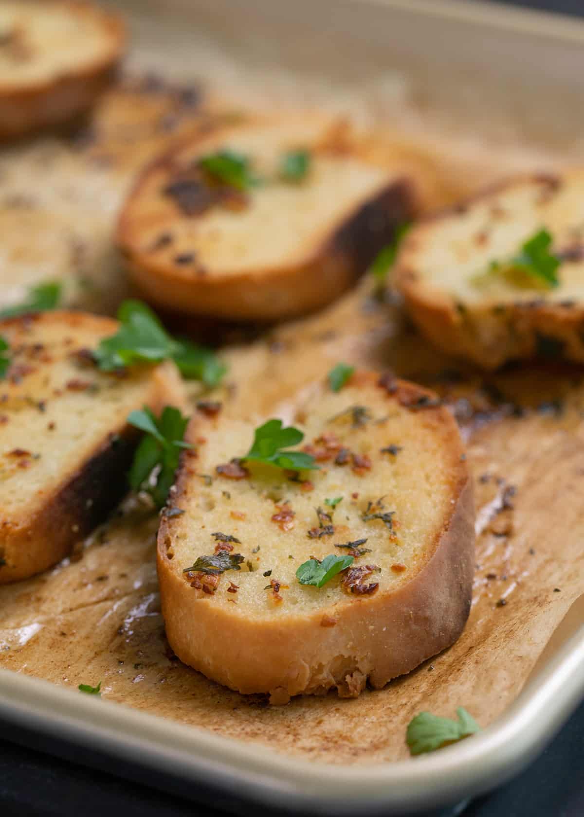 Pieces of garlic bread on baking sheet with fresh parsley leaves