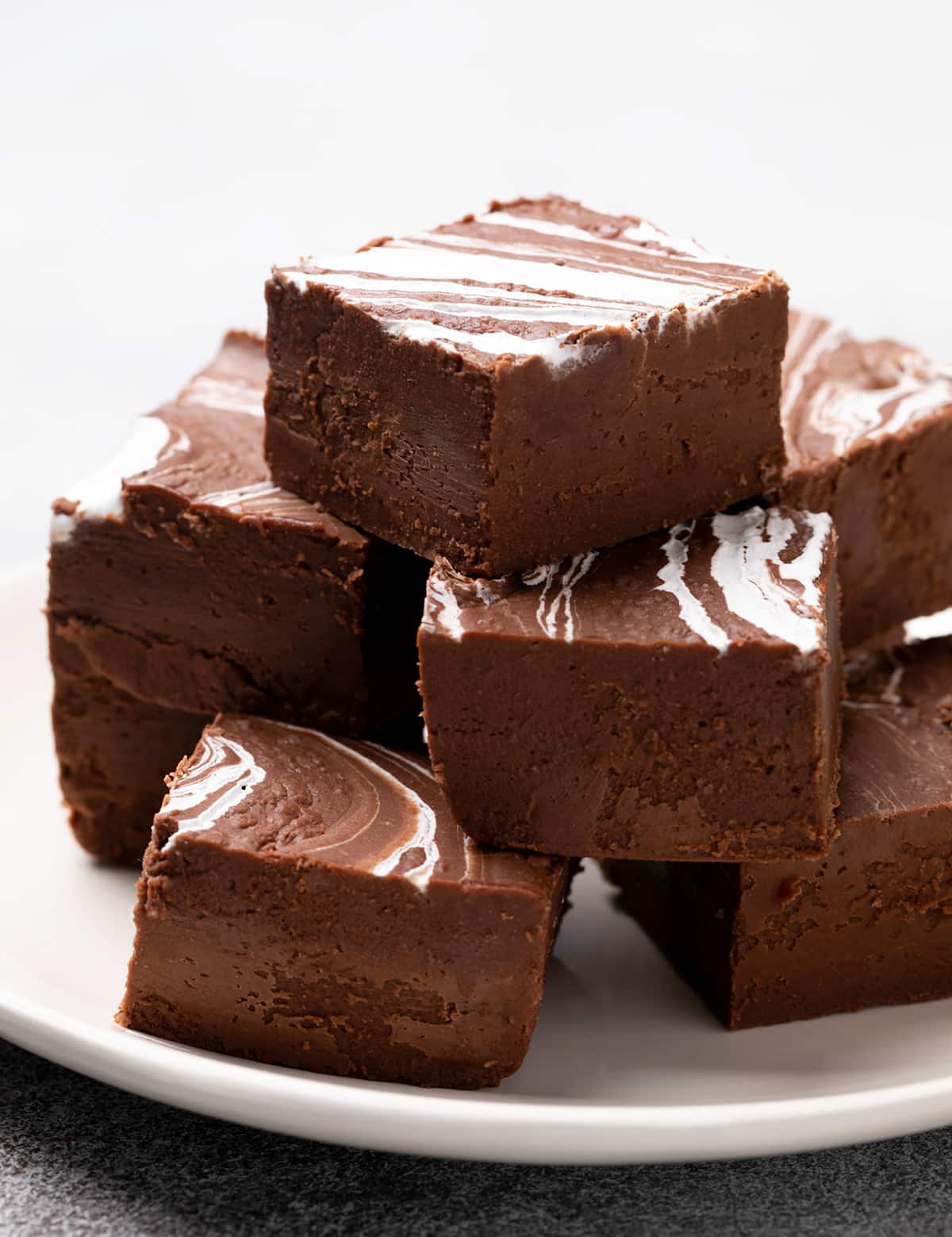 8 squares of brown fudge with white swirl on top arranged in stacked layers on small white plate