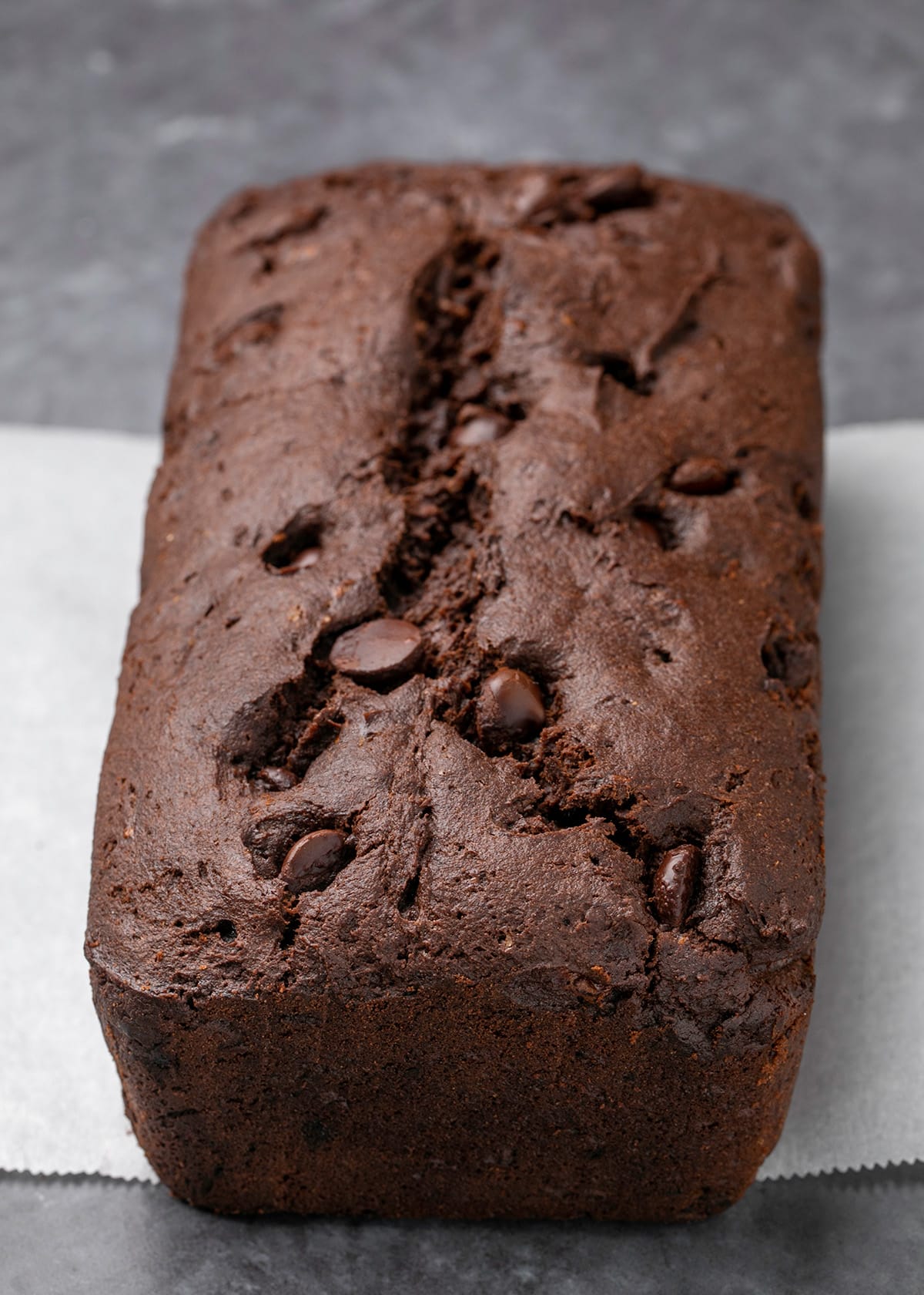 Brown loaf of cake with chocolate chips on slip of white paper on gray surface