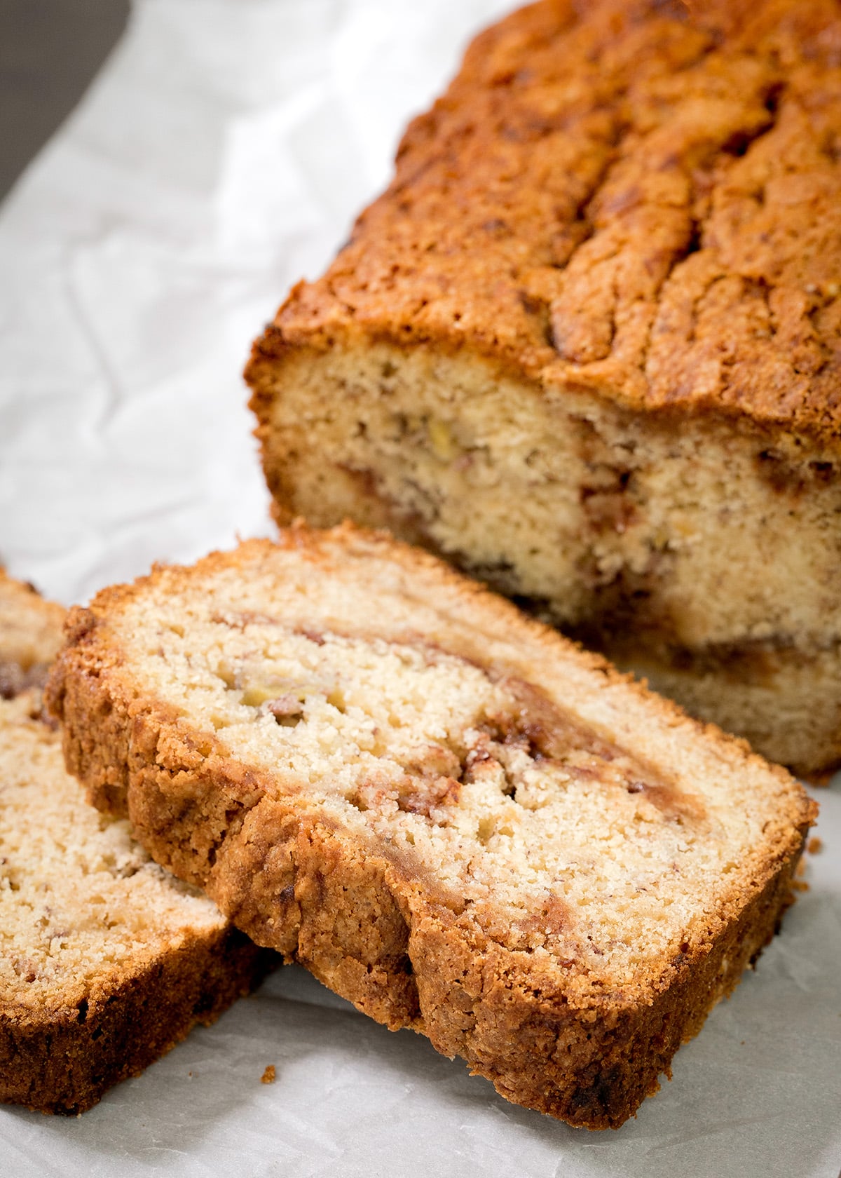 A thick slice of golden-brown bread rests in front of a cut loaf with dark swirls visible inside.