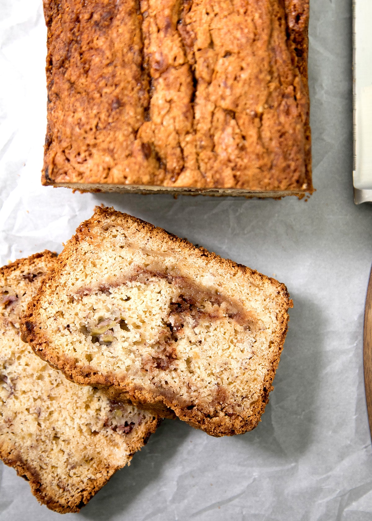 Overhead image of two slices of golden-brown bread overlap below a loaf, showing dark swirls through the crumb.
