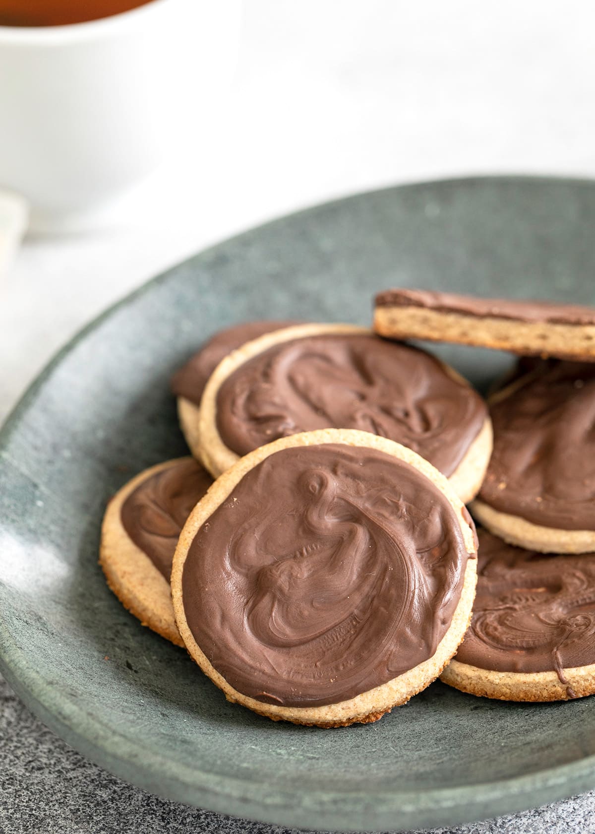 Digestive biscuits with chocolate coating on a gray plate with tea in background