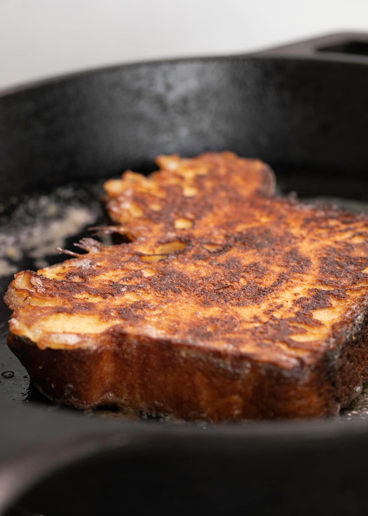 French toast slice frying in butter in black cast iron pan