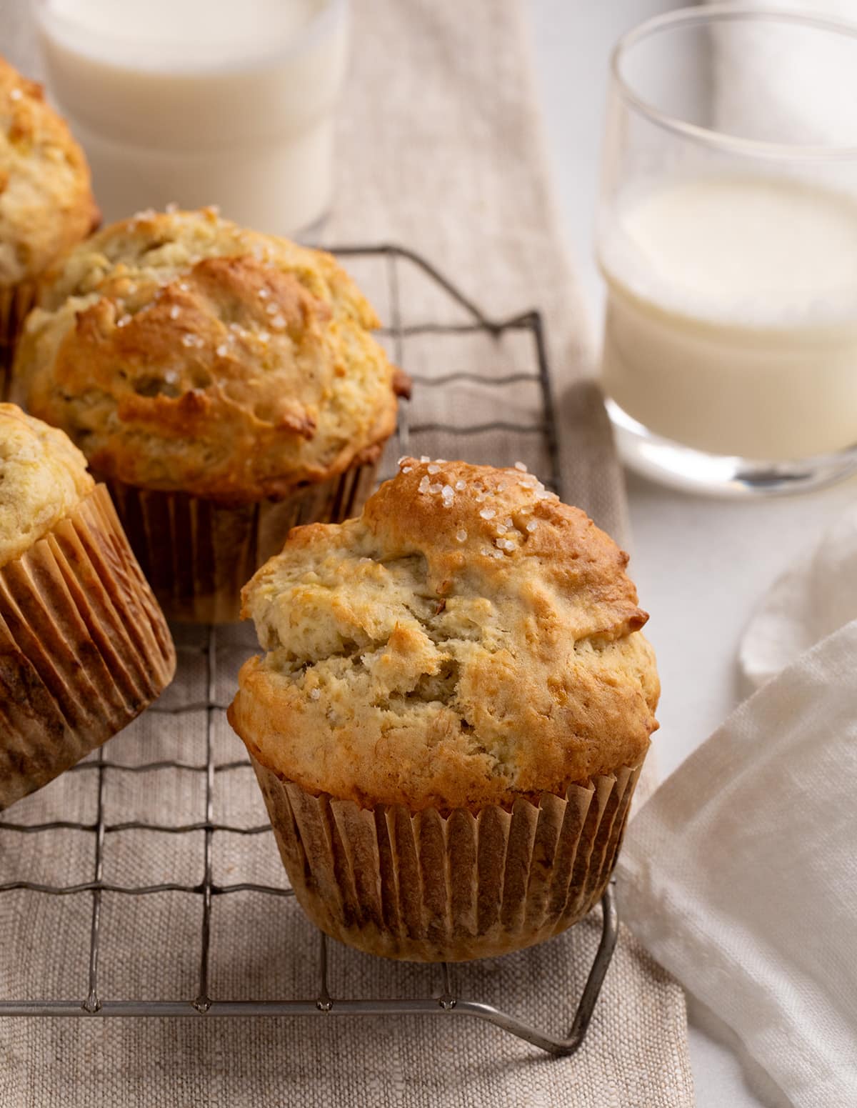 Golden-brown muffins rest on a wire cooling rack beside a glass of milk.
