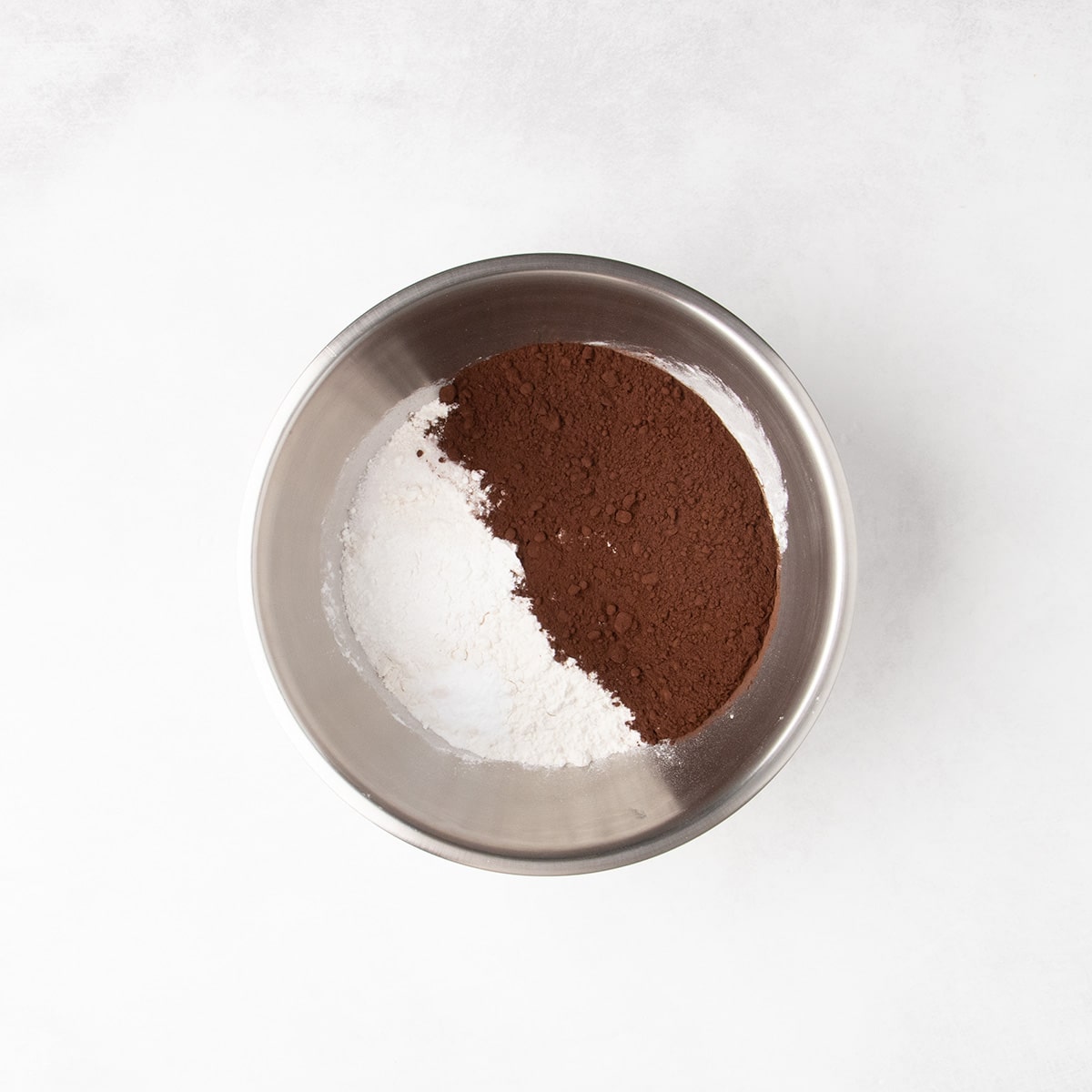 White and dark brown dry ingredients sit in separate piles in a stainless steel mixing bowl.