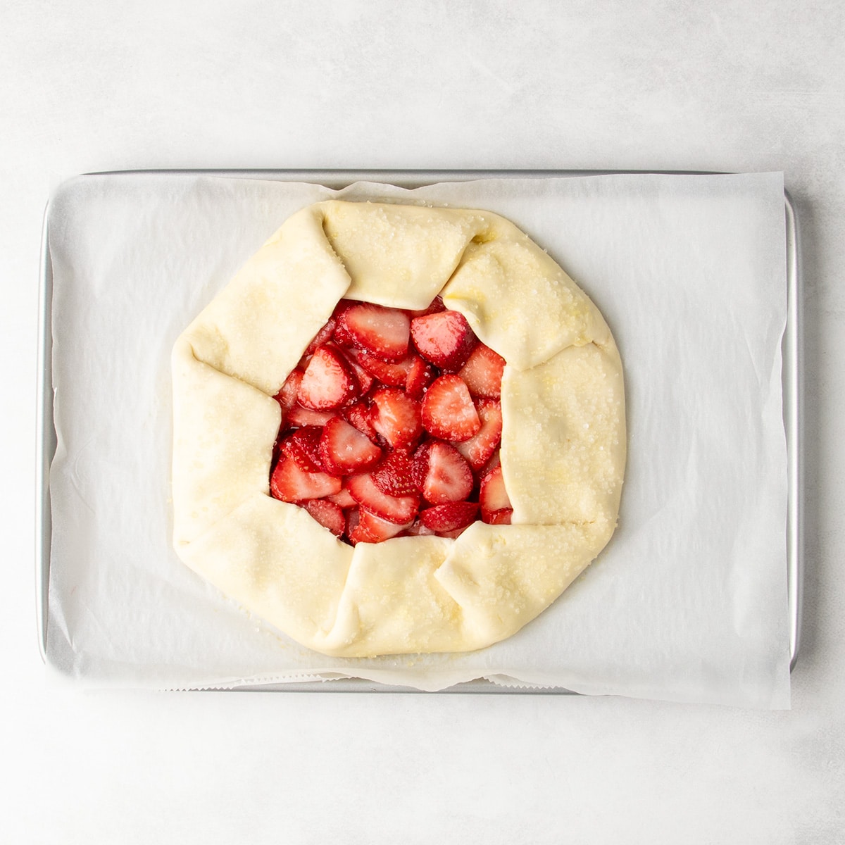 An unbaked strawberry galette sits on parchment paper on a rimmed baking sheet.