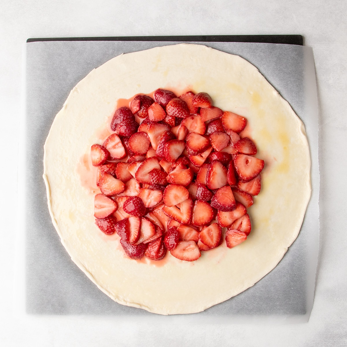 Sliced strawberries are piled in the center of a round sheet of dough on parchment paper.