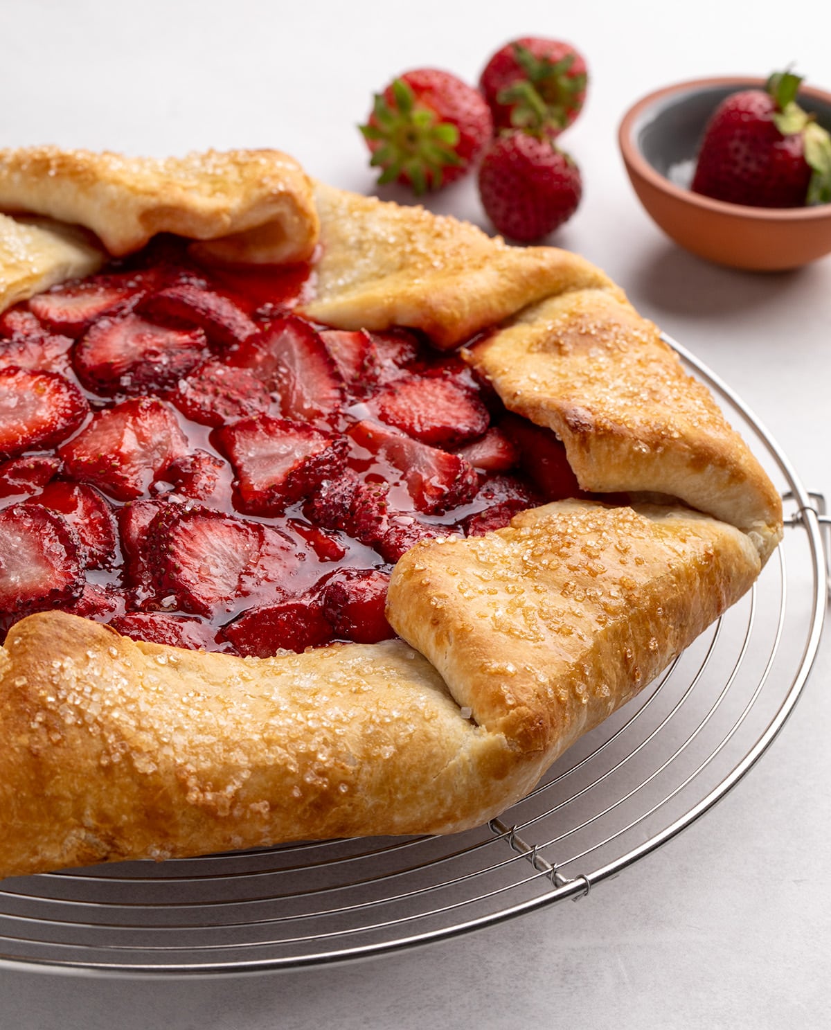 A full, uncut baked strawberry gluten free galette sits on a round wire rack with whole strawberries in the background.