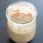 closeup image of light brown gluten free sourdough starter thick liquid light brown in jar on black surface