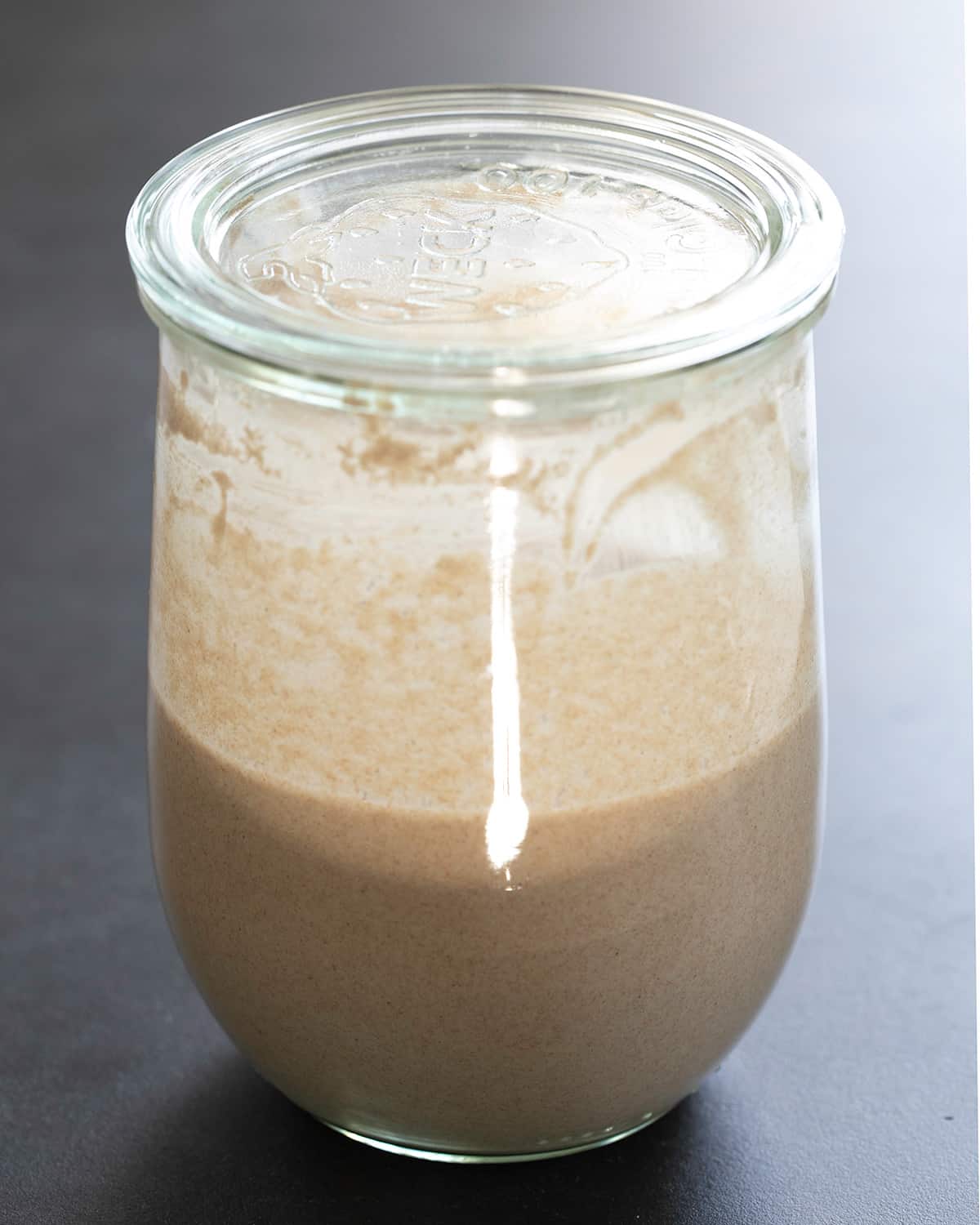 glass jar with recently fed gluten free sourdough starter with glass lid sitting on top