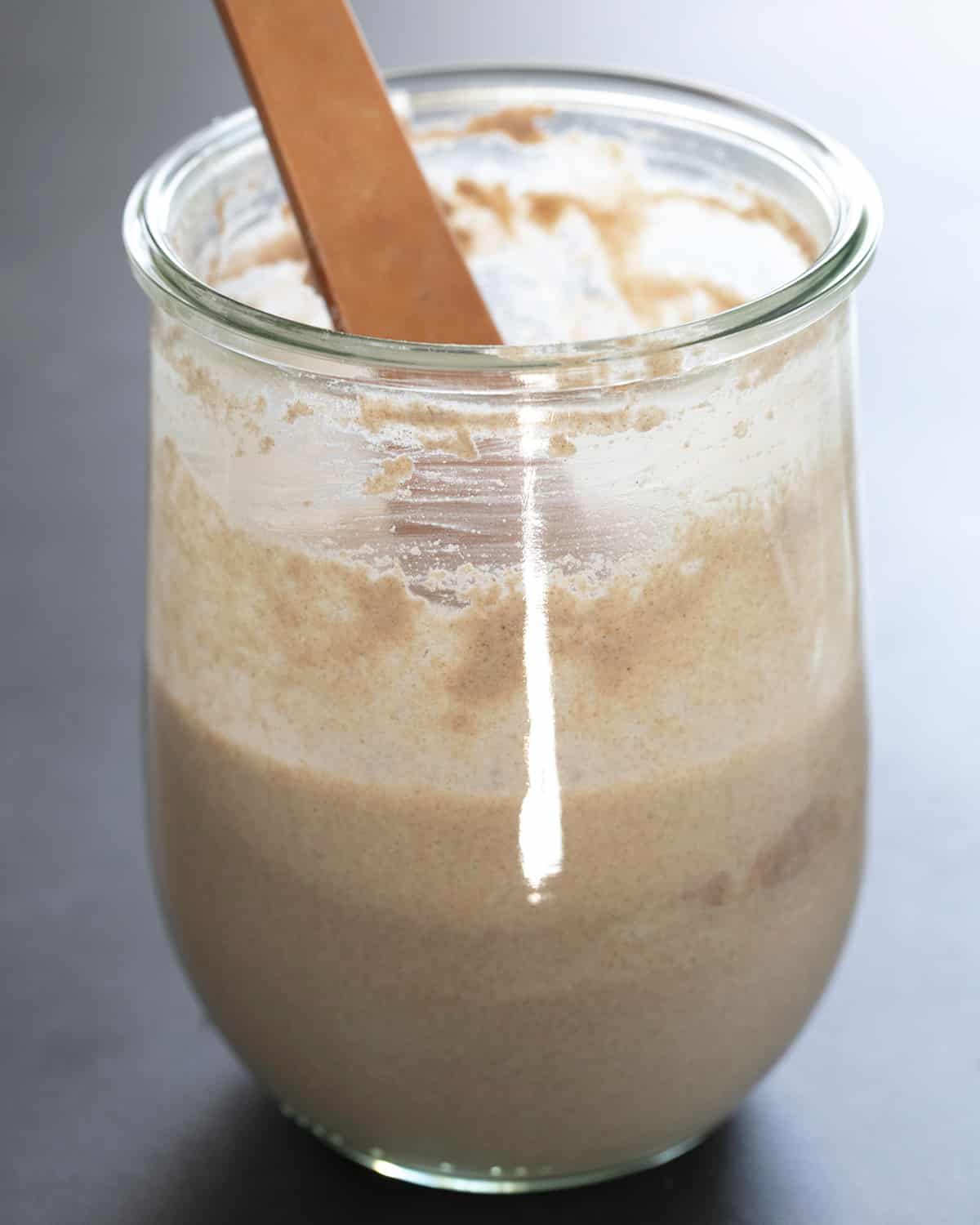 brown mixing spoon in glass jar of light brown sourdough starter