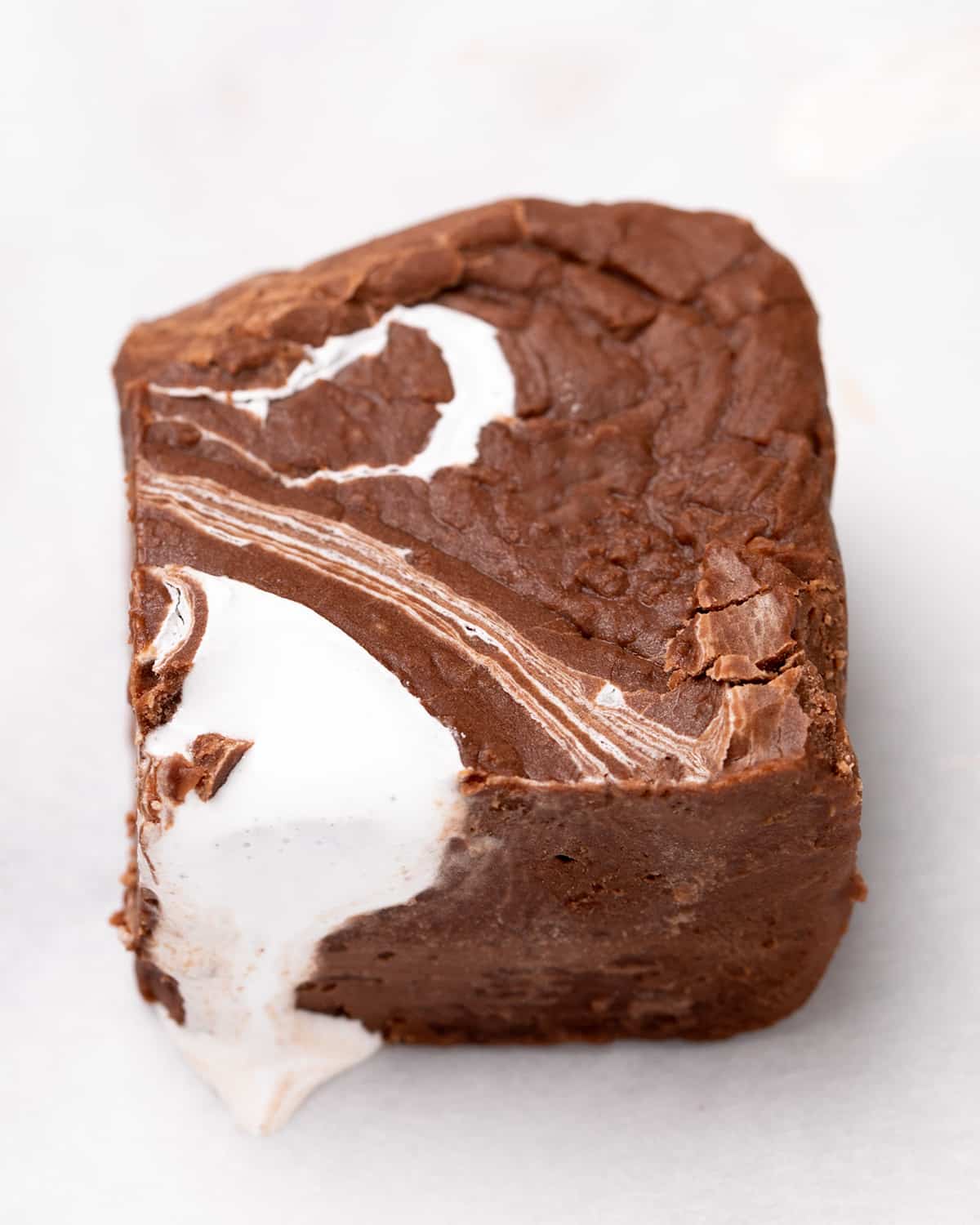 One piece of fudge with marshmallow fluff on top, dripping down the side on white paper