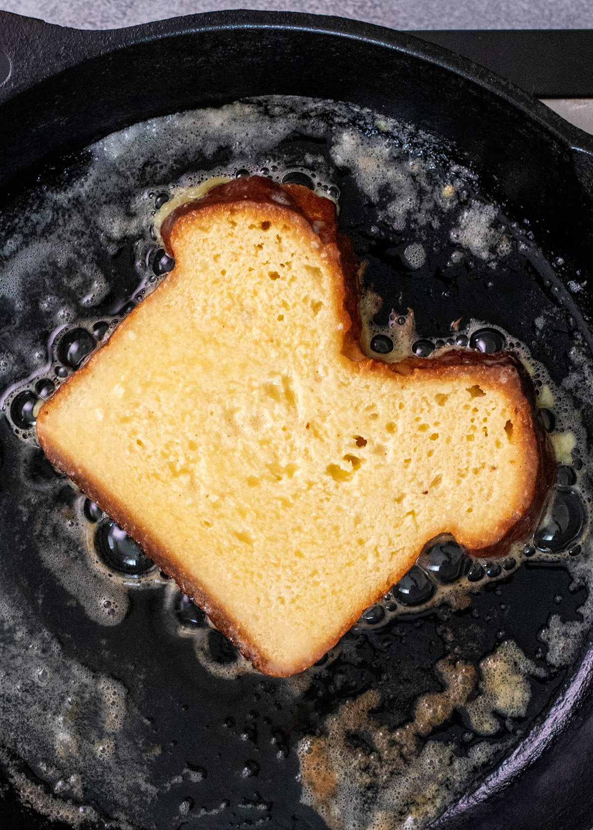 Overhead image of one slice of bread frying in a cast iron skillet with butter