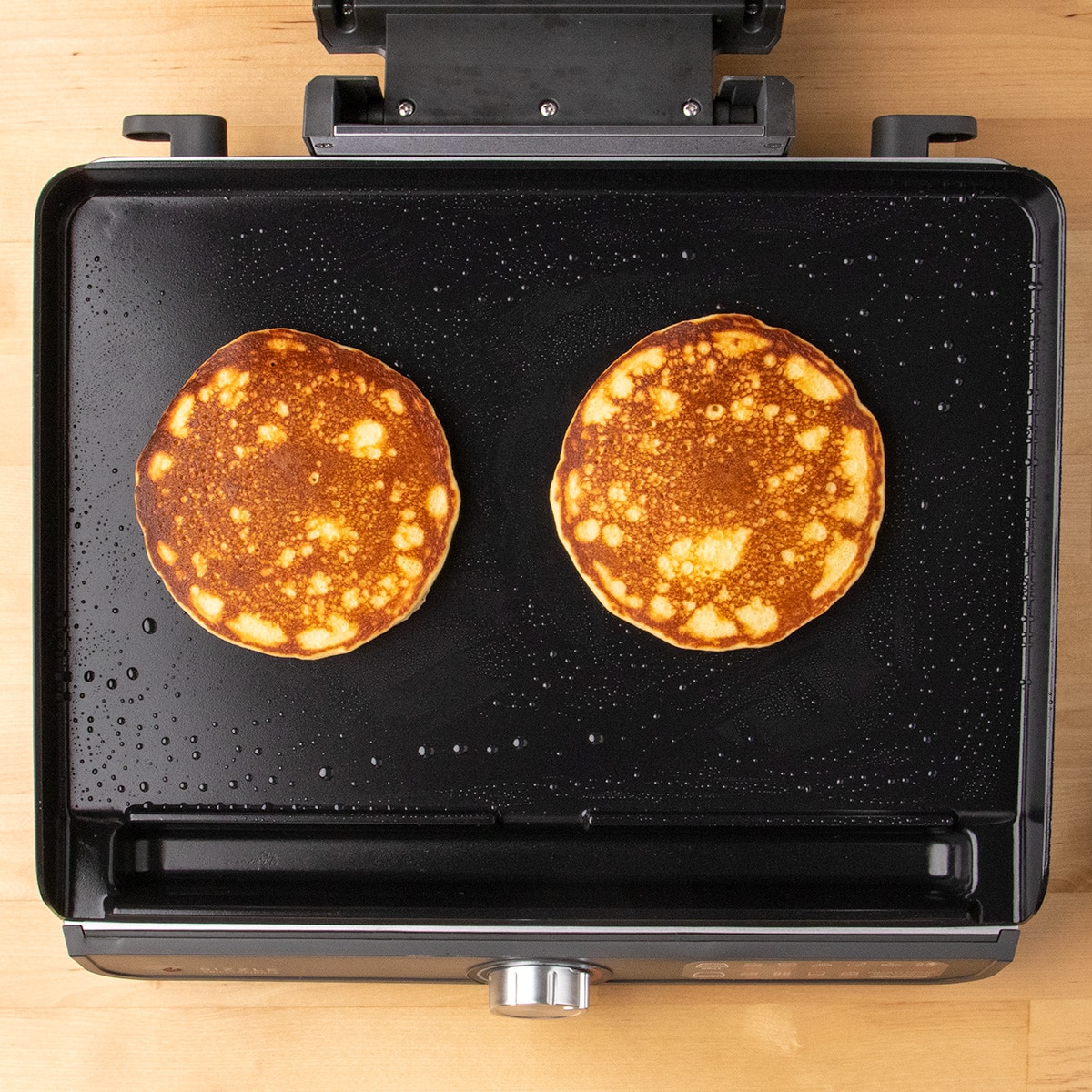 Two golden-brown pancakes cook side by side on a black griddle.