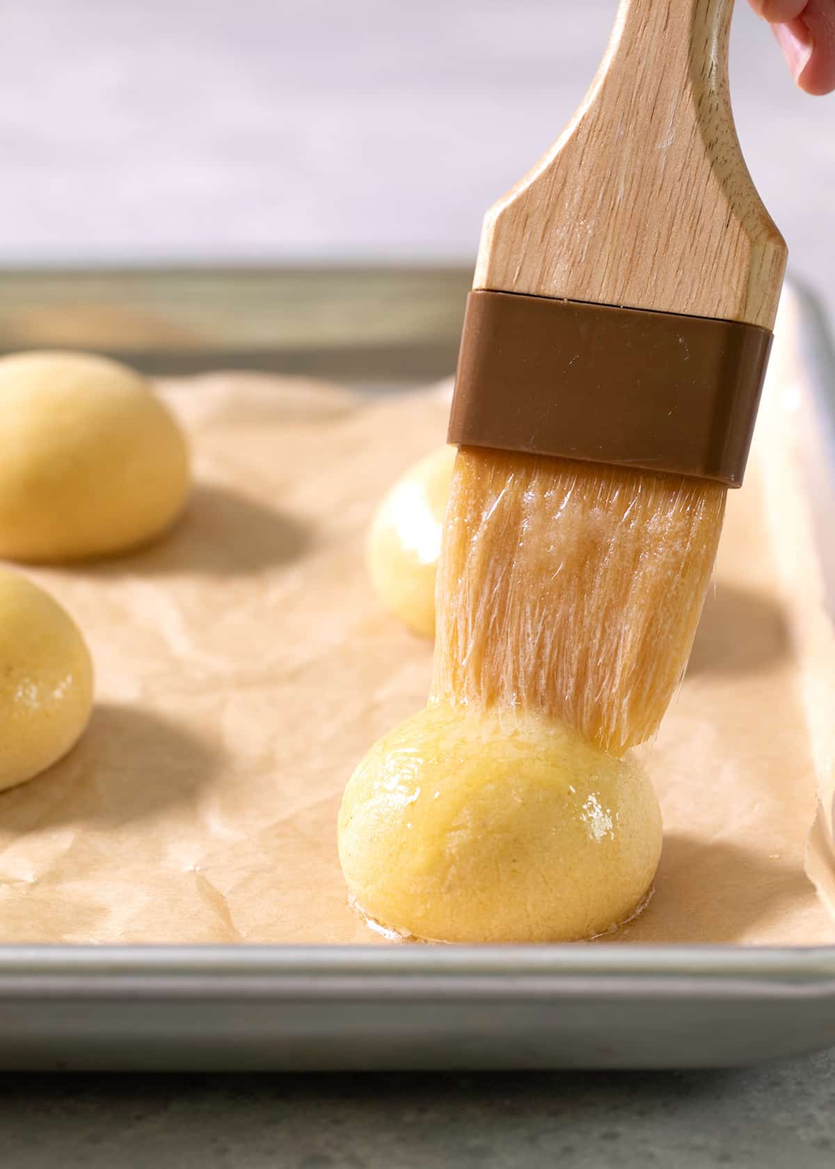 A pastry brush on top of a raw ball of pan de bono