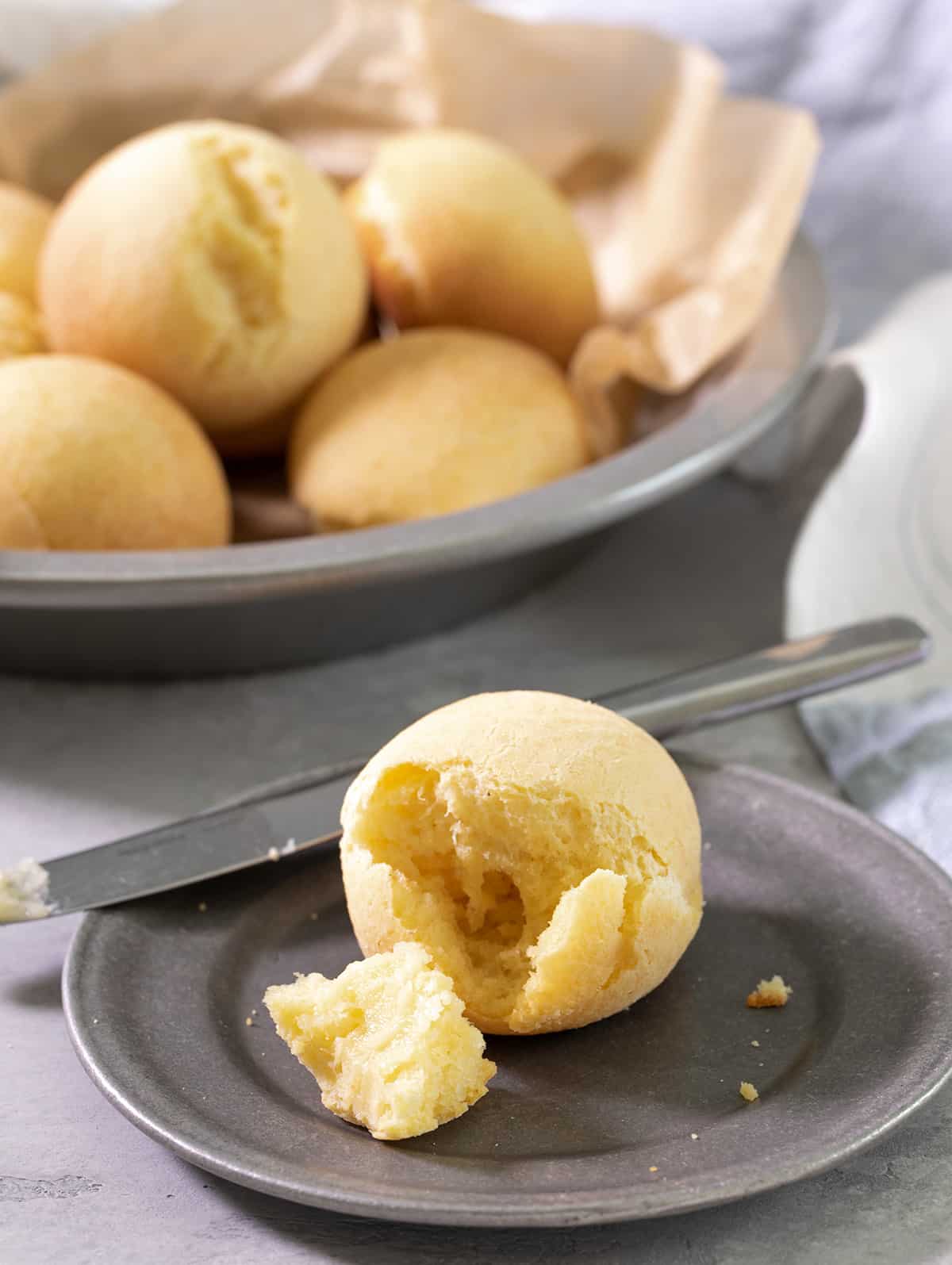A small plate with pan de bono broken, with a butter knife