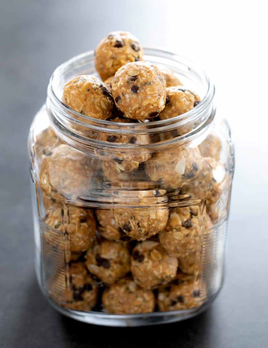 light brown oat protein balls with mini chocolate chips in large glass jar on black counter