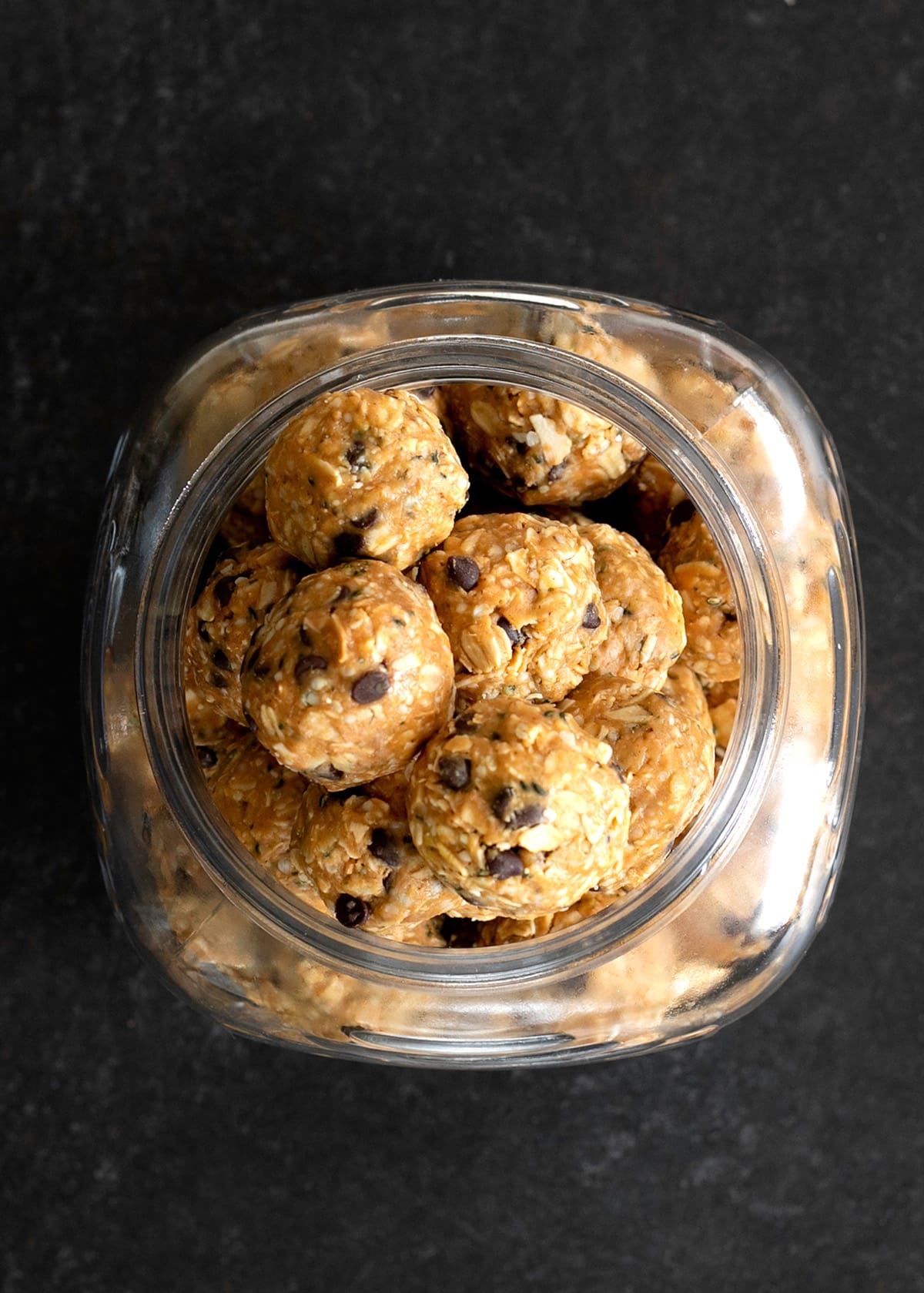 overhead image of protein balls with oats in glass jar on black surface