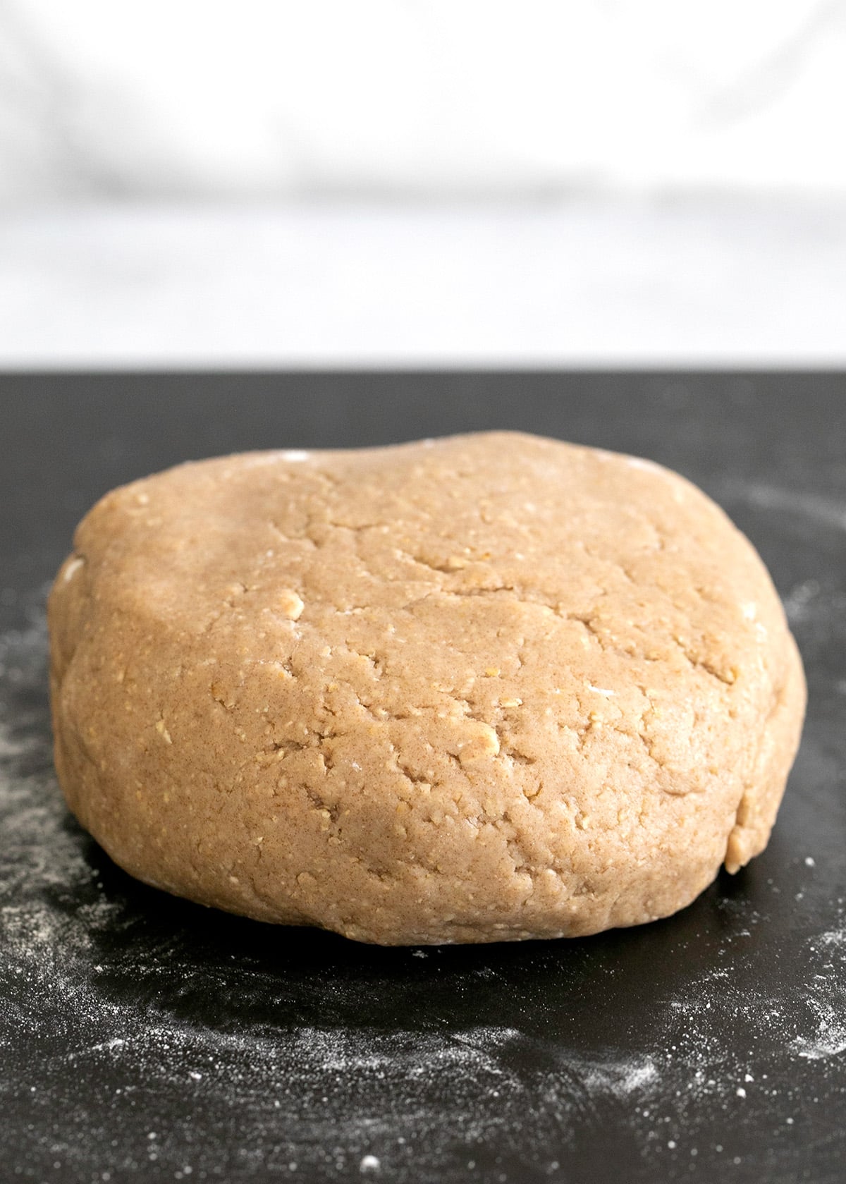 Raw digestive biscuit dough ball on black surface with white flour