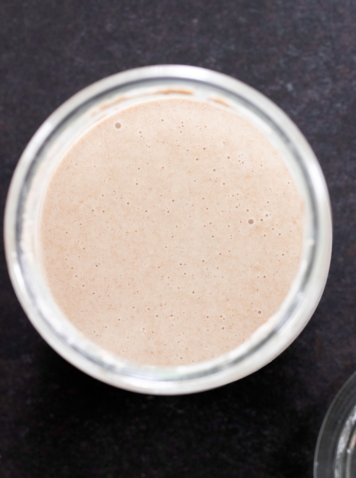 image from above of light brown liquid with small bubbles in it in glass jar on black surface