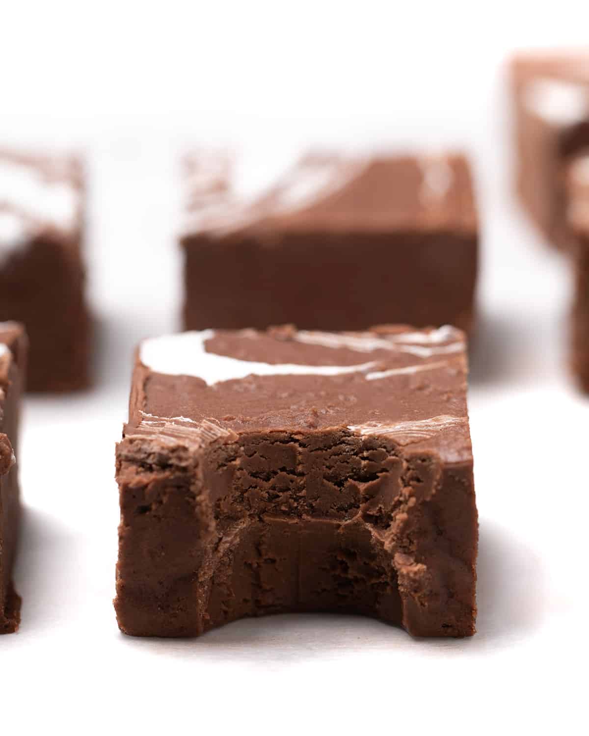 Squares of brown fudge on white paper, piece in center with bite taken