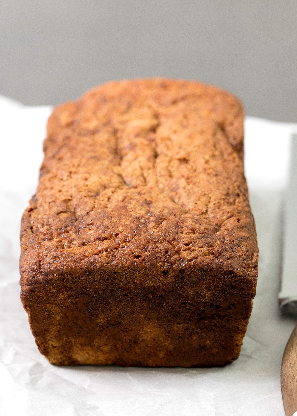 A whole rectangular loaf with a deeply browned, cracked top rests on parchment paper.