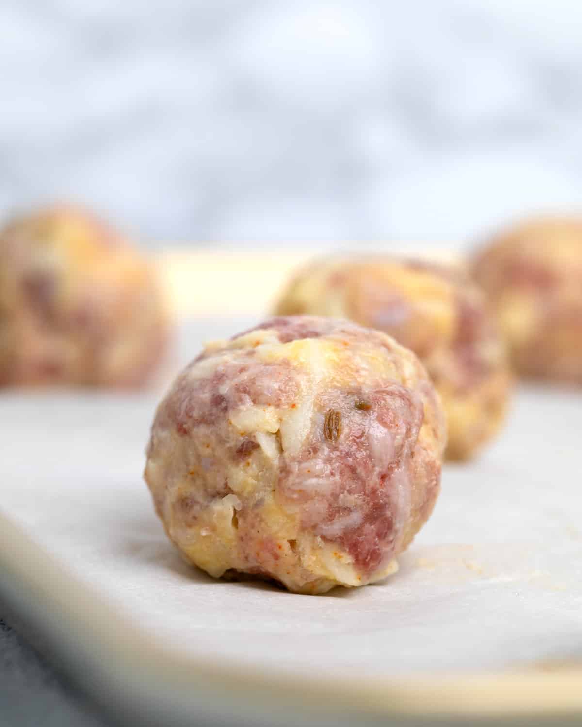 Closeup image of raw sausage ball on white paper on tray