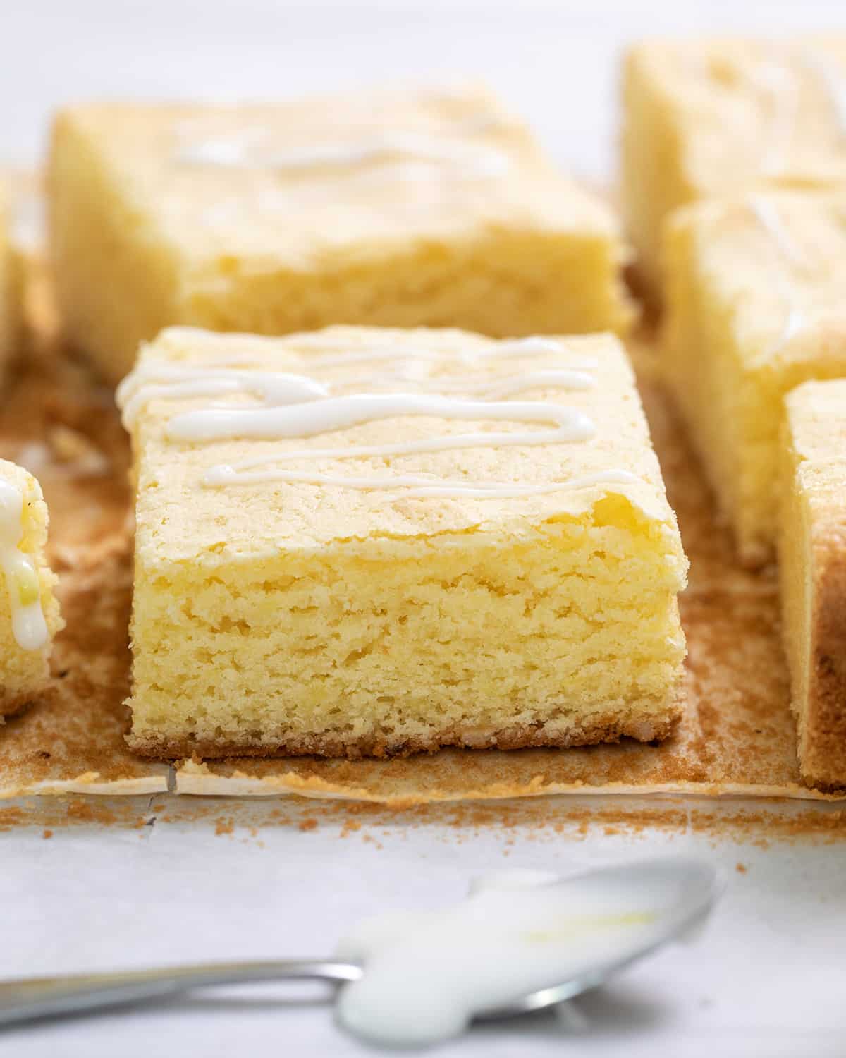 Cut lemon brownies on brown paper with a small spoon with icing in foreground