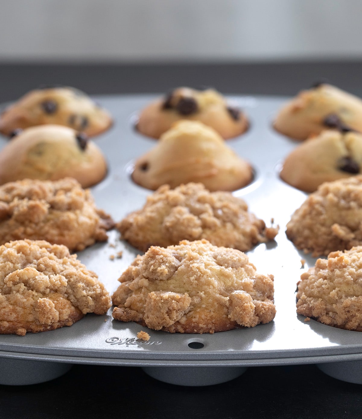 Closeup sideview of light colored crumble topping on gluten free muffins in metal muffin tin