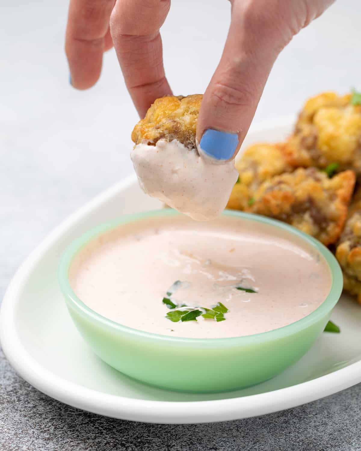 Fingers holding sausage ball dipped in light orange sauce
