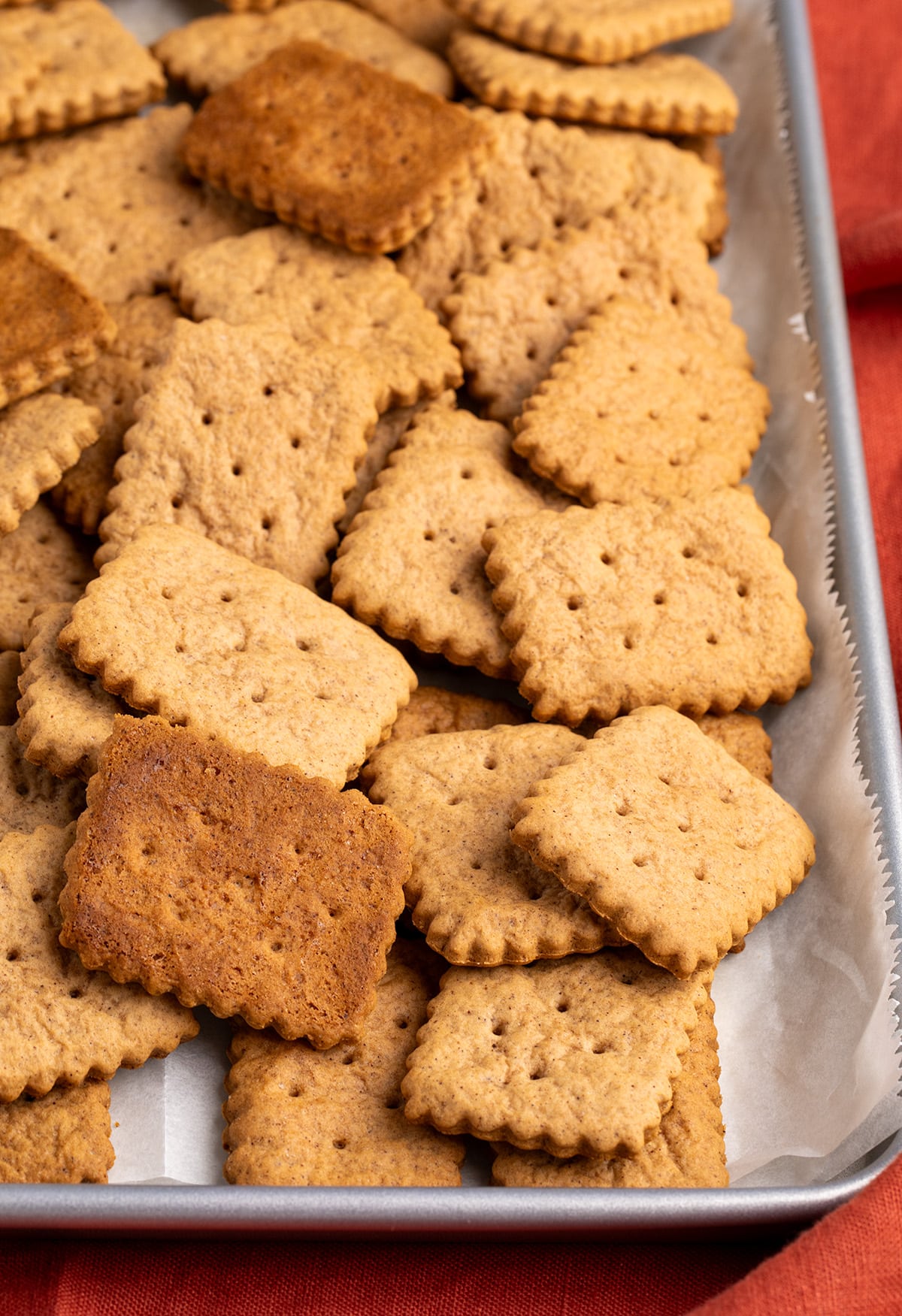 A close-up shows rectangular scalloped cookies piled on a parchment-lined baking sheet, including several darker cookies turned upside down.
