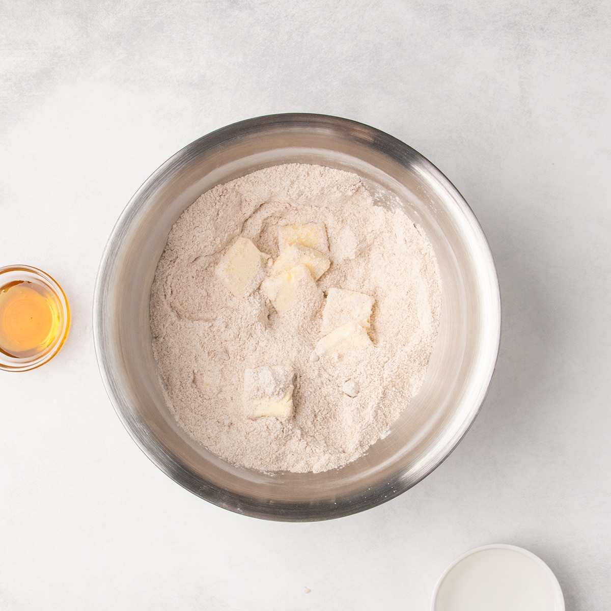 Squares of butter sit on top of the light brown dry ingredients in a large metal mixing bowl.