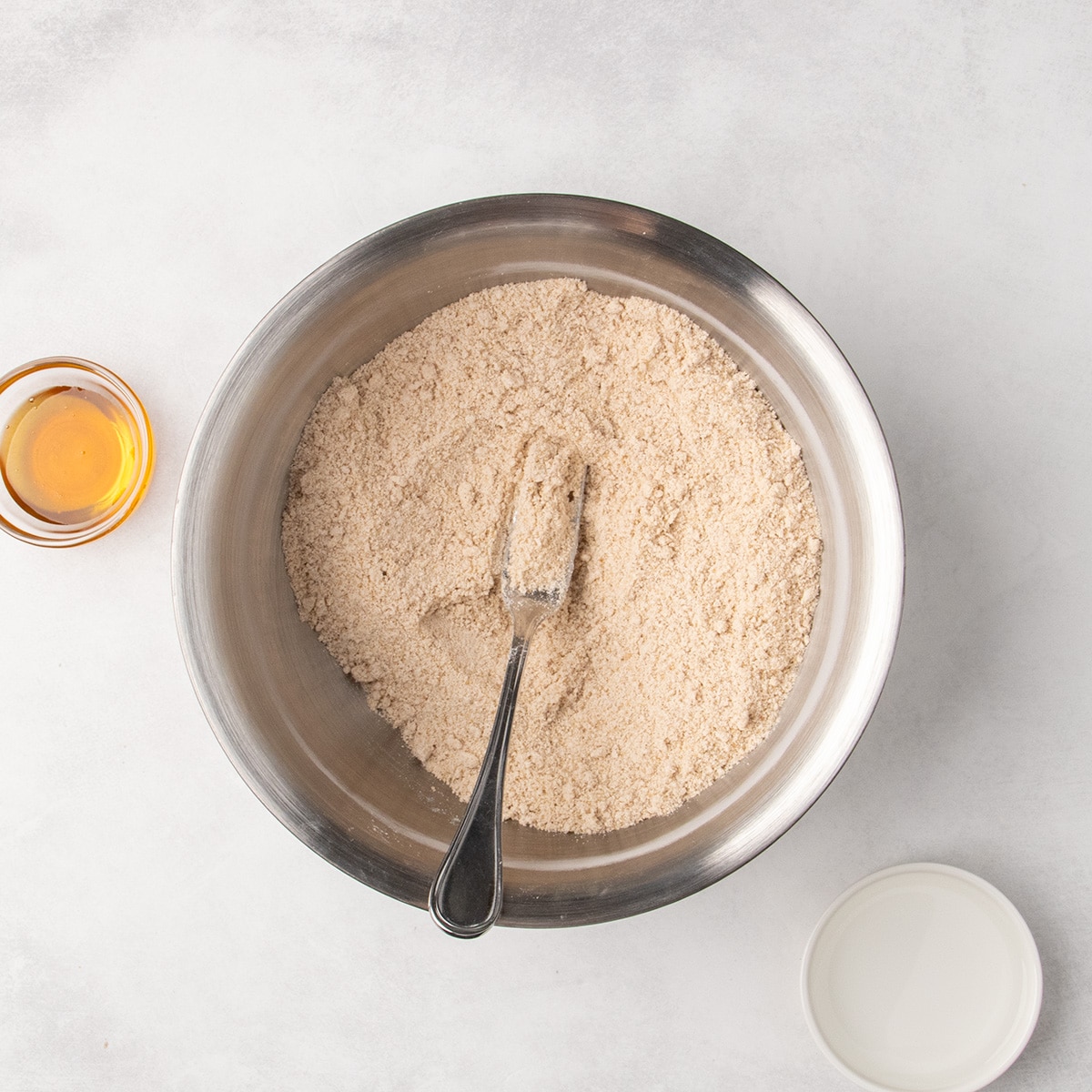 A fork rests in a sandy mixture of light brown dry ingredients and butter in a large metal mixing bowl.