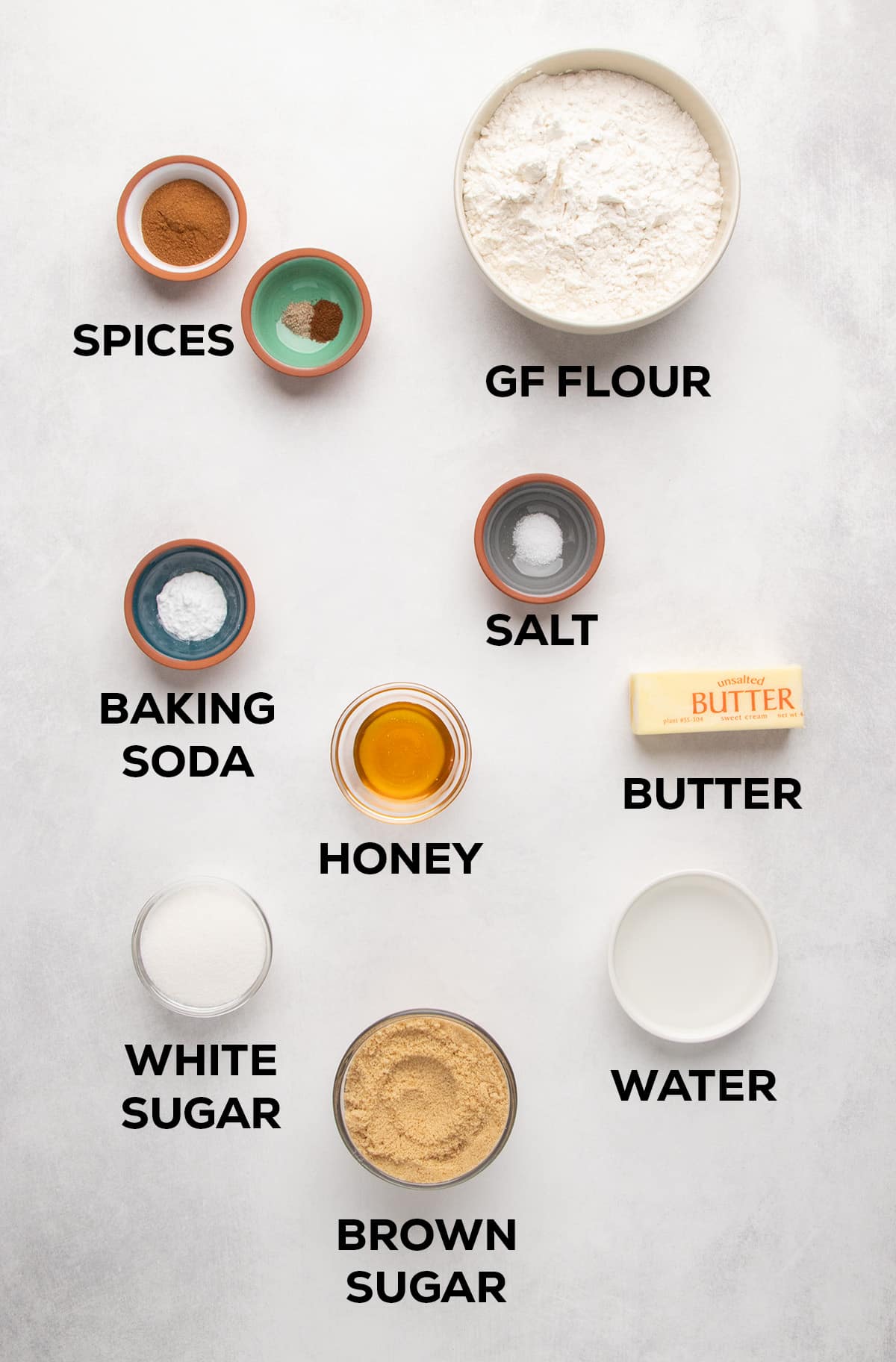 Labeled bowls and dishes show gluten free flour, spices, baking soda, salt, honey, butter, white sugar, brown sugar, and water.