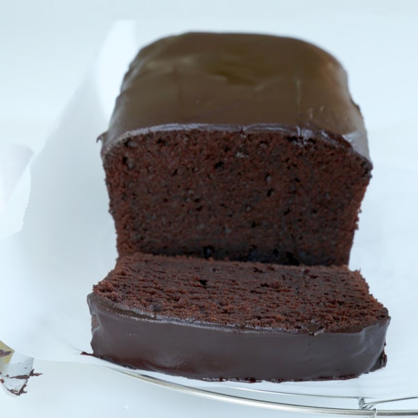closeup image of partially sliced gluten free chocolate pound cake loaf, with chocolate icing on top and a knife on the side