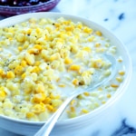 closeup image of creamed gluten free yellow corn in white sauce in wide white bowl with serving spoon