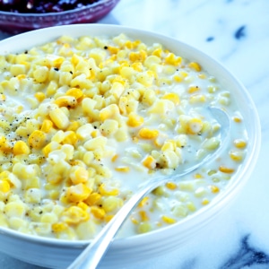 closeup image of creamed gluten free yellow corn in white sauce in wide white bowl with serving spoon