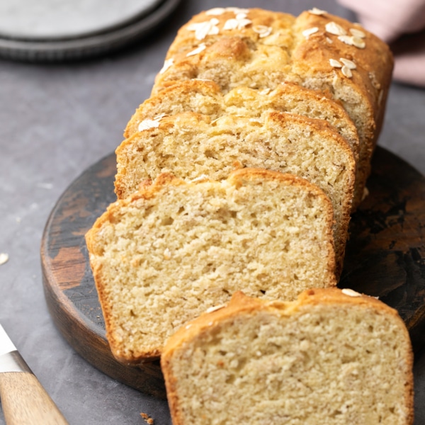closeup image of sliced gluten free oat bread on round dark wood cutting board