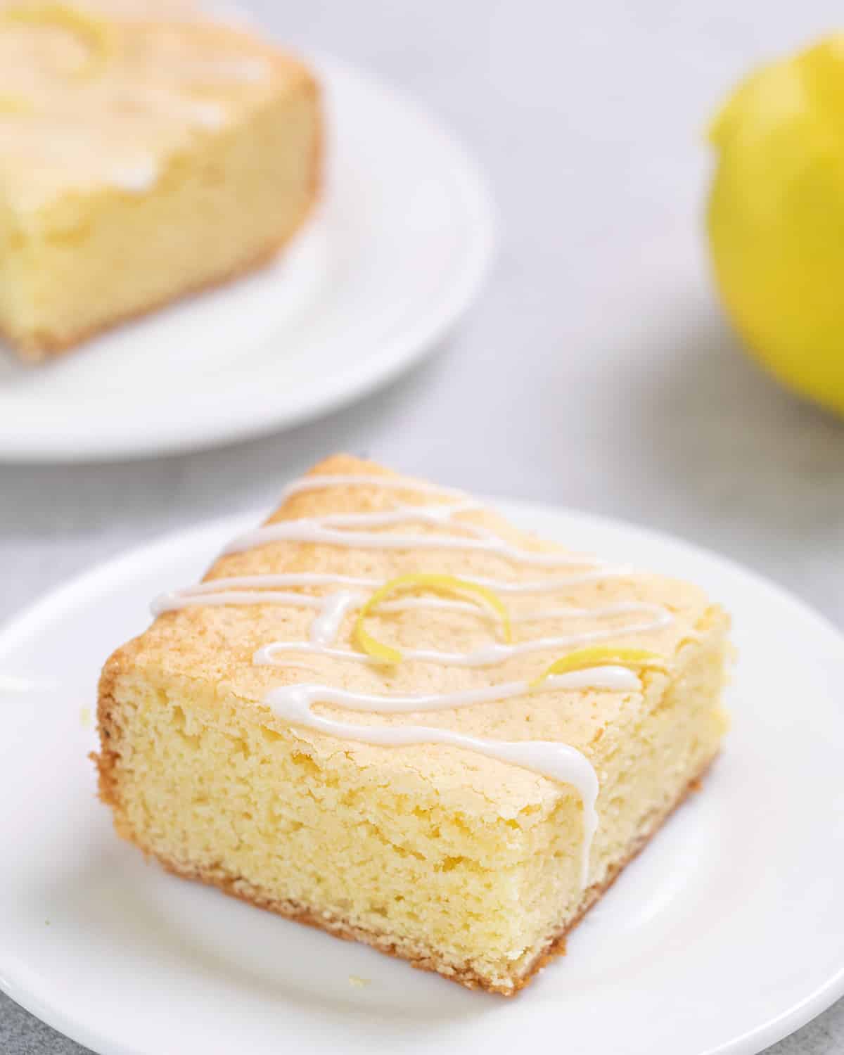 Lemon brownie with icing drizzle and some lemon zest on small white plate
